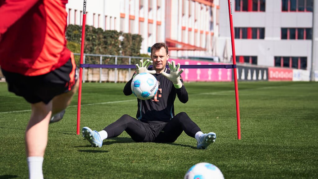 Bayern Munich goalkeeper Manuel Neuer sitting on the grass and catching a ball during training