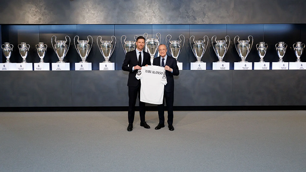 Xabi Alonso and Real Madrid president holding a Madrid shirt in front of trophies won by the club