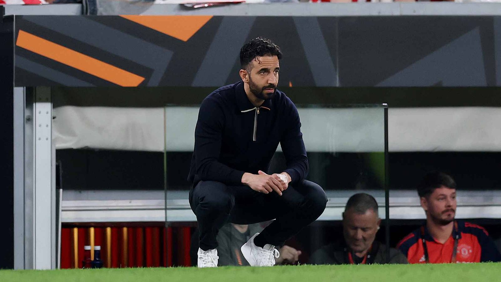 Manchester United coach Ruben Amorim squatting on the touchline and looking on during a match