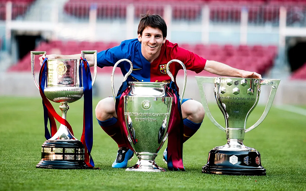 Lionel Messi posing with three trophies in a Barcelona shirt