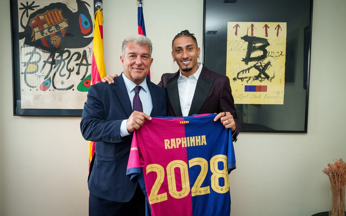 Raphinha holding up a Barcelona shirt with club president Laporta