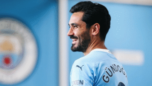 Ilkay Gundogan posing in a Manchester City shirt with club logo on the wall