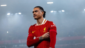 Darwin Nunez in a Liverpool shirt walking under floodlights at Anfield at nighttime