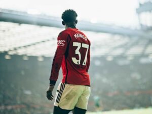 Manchester United midfielder Kobbie Mainoo standing in a stadium in daytime