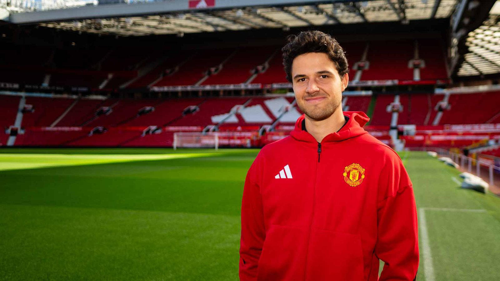 Senne Lammens standing inside Old Trafford wearing a red Manchester United jacket
