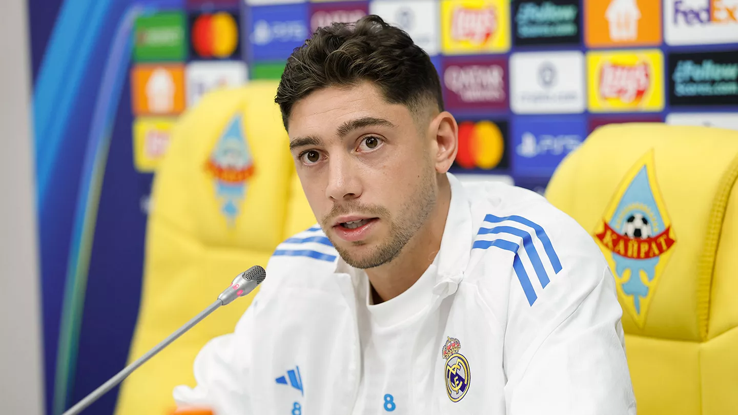 Federico Valverde in a white Real Madrid tracksuit sitting in a news room and speaking to the media
