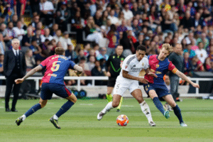 Real Madrid player Jude Bellingham holding off Barcelona players Frenkie de Jong and Inigo Martinez