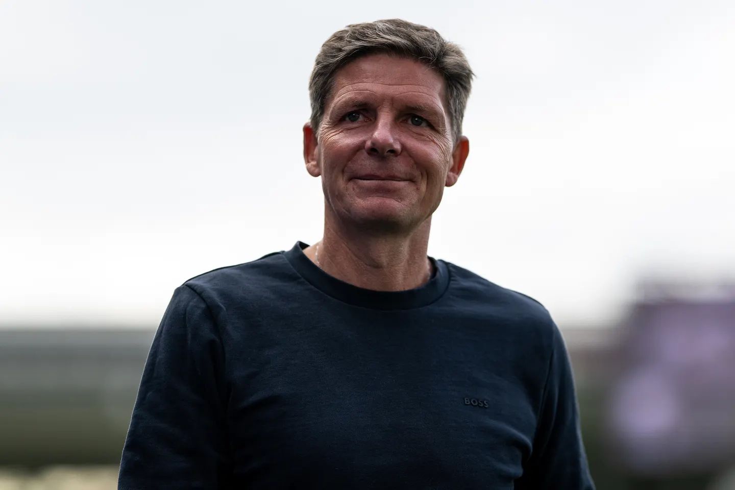 Oliver Glasner in a black t-shirt standing against the grey sky