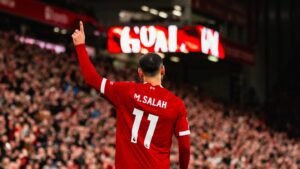 Liverpool forward Mohamed standing and raising arm in front of Anfield crowd