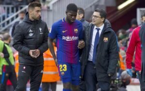 Samuel Umtiti holding the back of his knee while being escorted by Barcelona staff after sustaining another injury