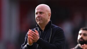 Arne Slot applauding on the sidelines after a Liverpool match at Anfield, with Mohamed Salah in the background