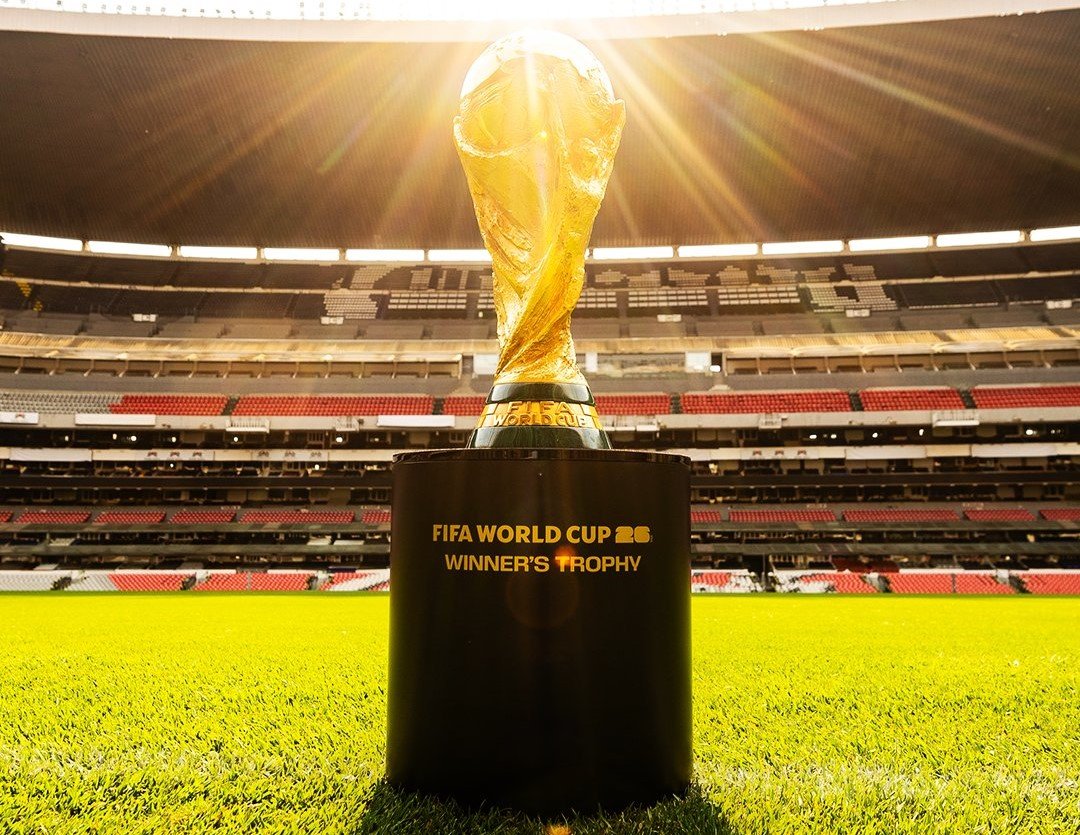 World Cup trophy standing on a plinth in a stadium with sun rays streaming behind it