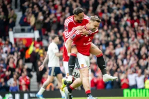 Manchester United left-back Luke Shaw celebrating goal with teammate Matheus Cunha climbing atop his back