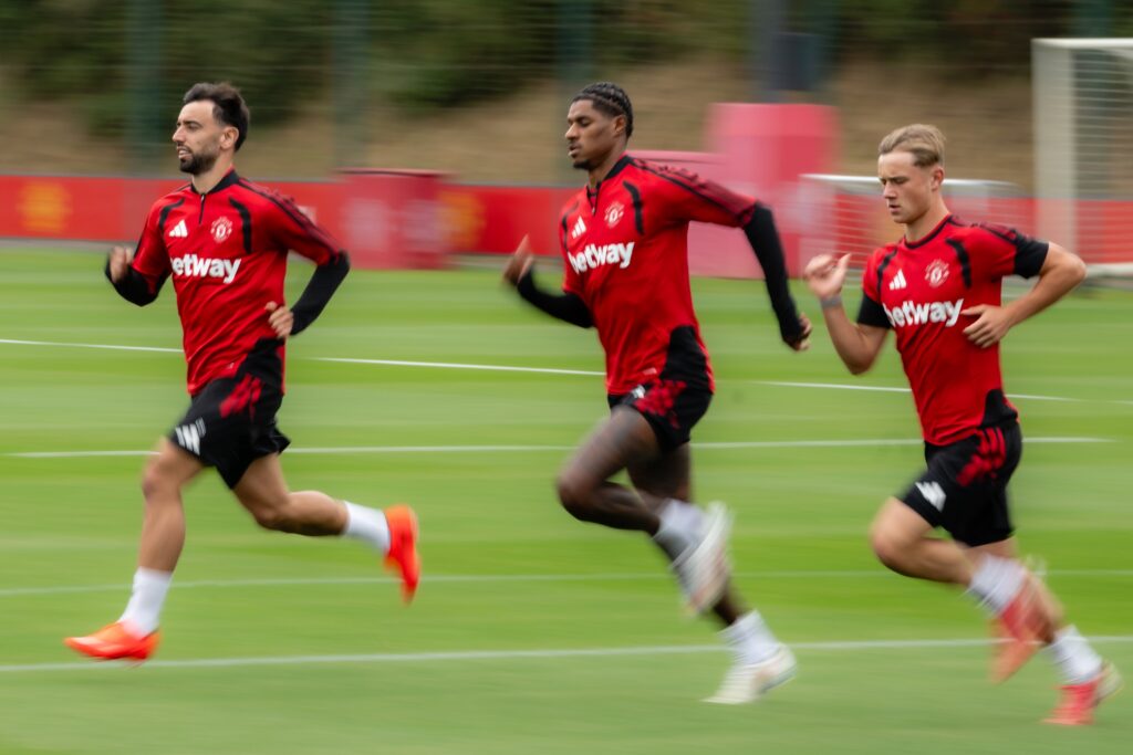Manchester United captaining Bruno Fernandes running on the training ground alongside Marcus Rashford and another teammate