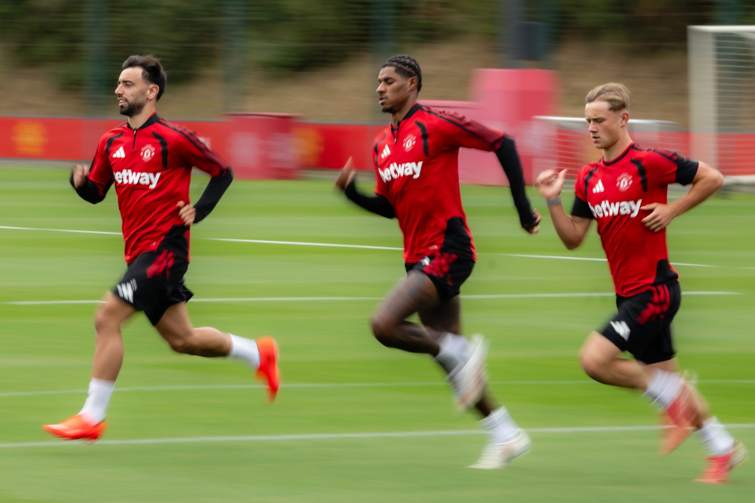 Manchester United captaining Bruno Fernandes running on the training ground alongside Marcus Rashford and another teammate