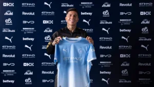 Enzo Fernandez holding up a Manchester City jersey